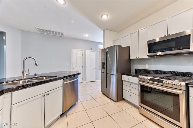 kitchen with appliances with stainless steel finishes, light tile patterned flooring, sink, white cabinetry, and dark stone counters