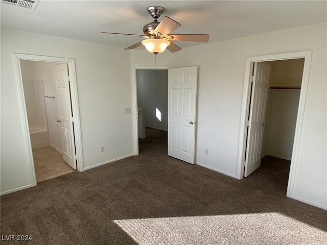 unfurnished bedroom featuring connected bathroom, a closet, dark carpet, a spacious closet, and ceiling fan