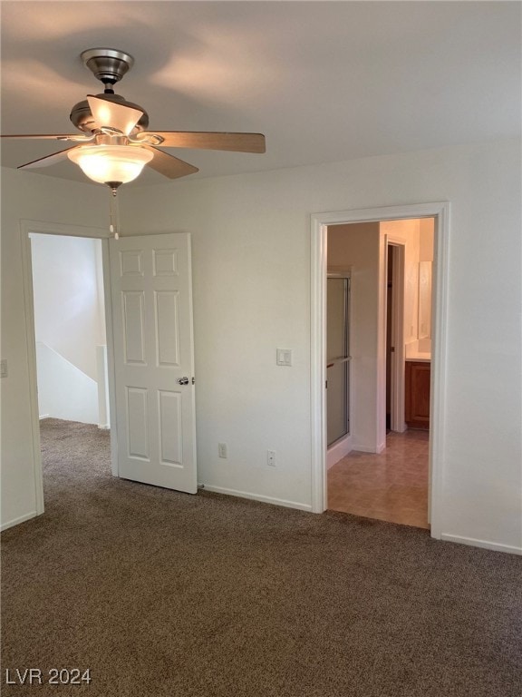 unfurnished bedroom featuring dark carpet, ensuite bathroom, and ceiling fan