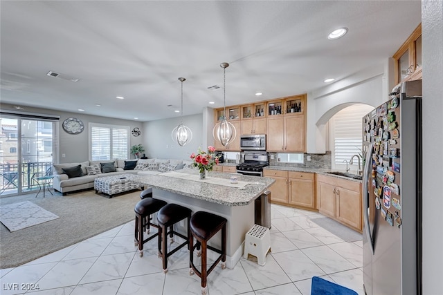 kitchen with a breakfast bar, sink, a kitchen island, light stone counters, and stainless steel appliances