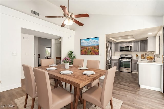 dining room with hardwood / wood-style floors, ceiling fan, sink, and vaulted ceiling