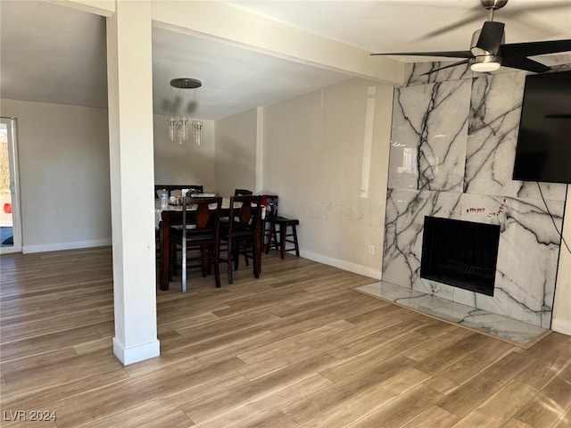 dining space with ceiling fan with notable chandelier, hardwood / wood-style flooring, beamed ceiling, and a high end fireplace