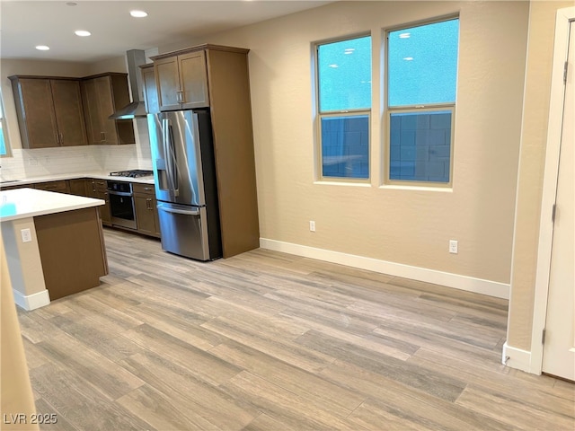 kitchen with decorative backsplash, appliances with stainless steel finishes, sink, wall chimney range hood, and light hardwood / wood-style floors