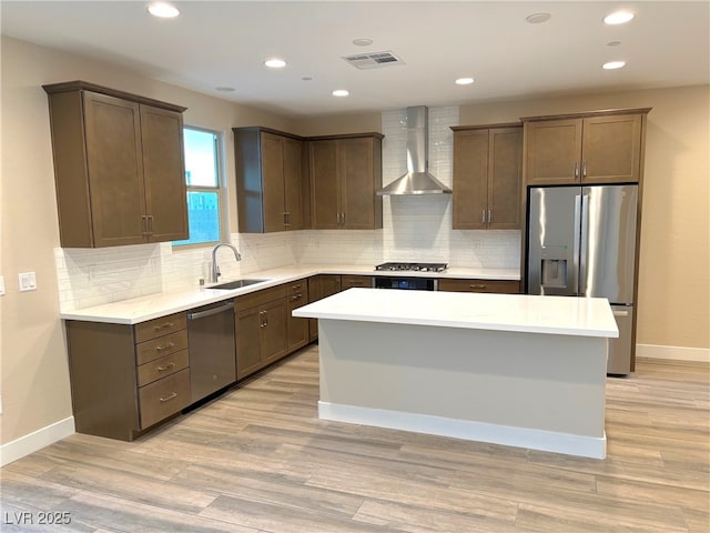 kitchen with a center island, sink, wall chimney exhaust hood, light hardwood / wood-style flooring, and appliances with stainless steel finishes