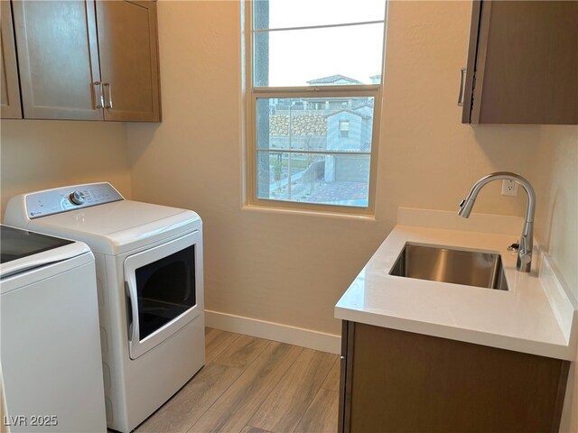 laundry area featuring cabinets, light hardwood / wood-style flooring, washer and clothes dryer, and sink