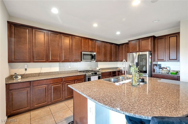 kitchen featuring an island with sink, light stone countertops, sink, and appliances with stainless steel finishes