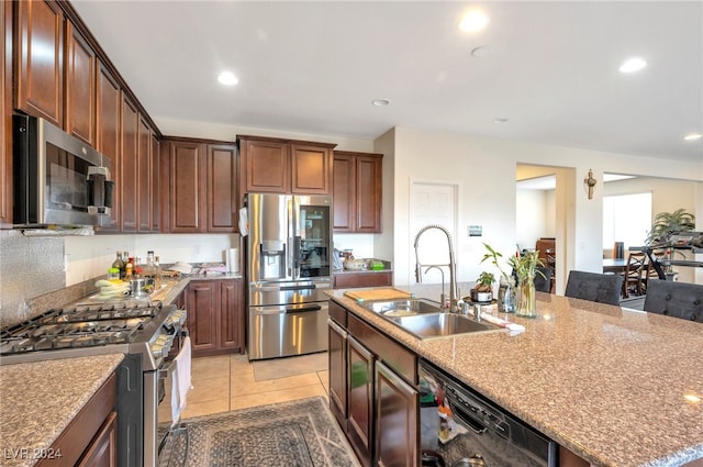 kitchen with sink, appliances with stainless steel finishes, light stone countertops, light tile patterned floors, and a kitchen island with sink