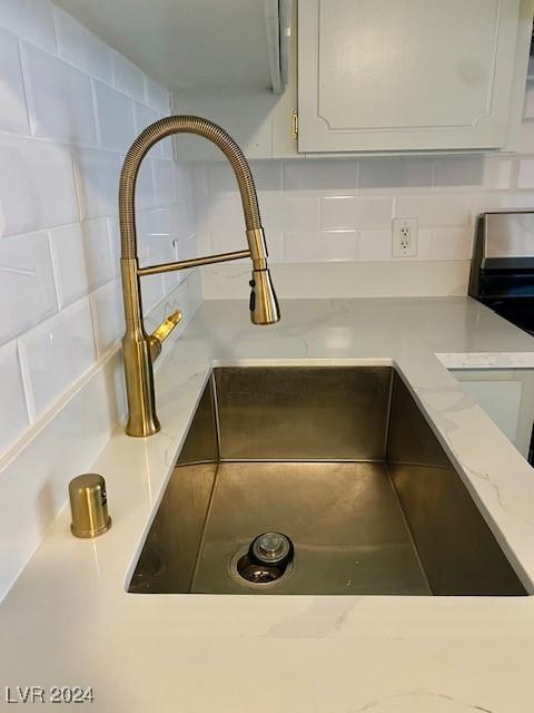 details featuring white cabinets, sink, backsplash, and light stone counters