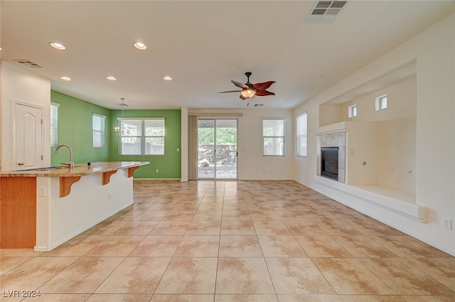 unfurnished living room featuring a tile fireplace, ceiling fan with notable chandelier, and light tile patterned flooring