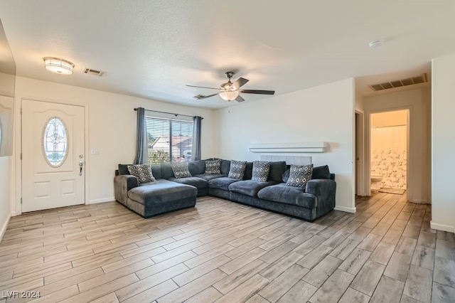 living room with a textured ceiling, light wood-type flooring, and ceiling fan