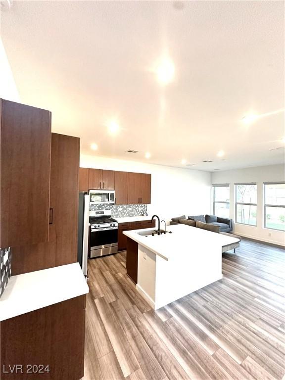 9847 Kings Glen St, Las Vegas, NV 89141 - kitchen featuring stainless steel appliances, a sink, open floor plan, light wood-style flooring, and an island with sink