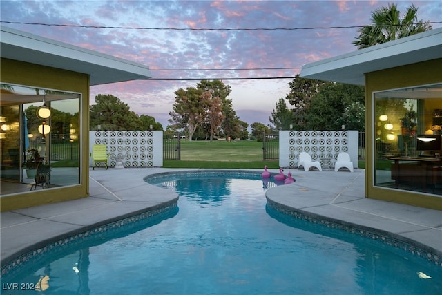 pool at dusk featuring a lawn and a patio