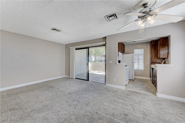 interior space with white appliances, a textured ceiling, light carpet, ceiling fan, and dark brown cabinetry