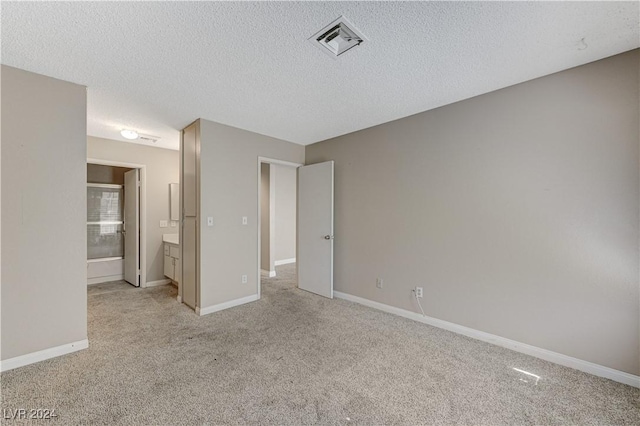 unfurnished bedroom featuring ensuite bath, light colored carpet, and a textured ceiling