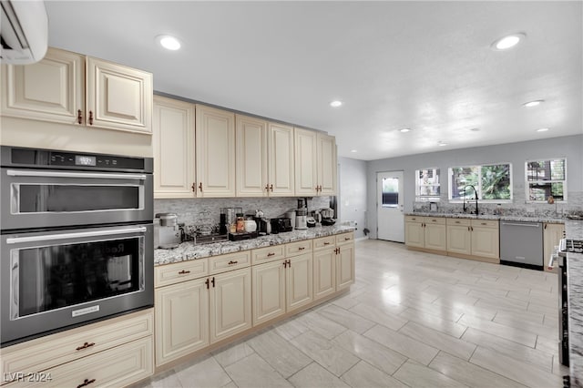 kitchen with cream cabinets, backsplash, appliances with stainless steel finishes, light stone countertops, and sink