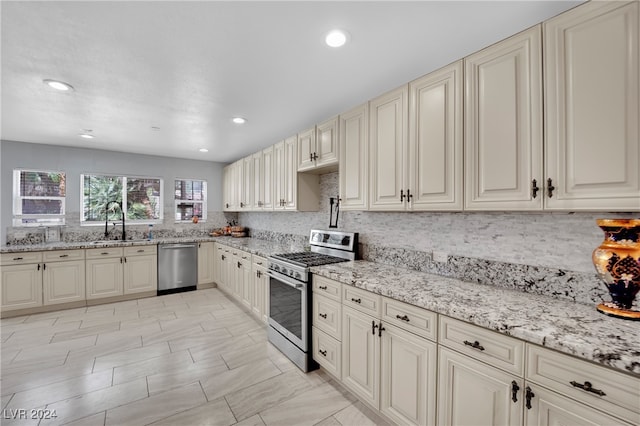 kitchen featuring cream cabinets, stainless steel appliances, backsplash, sink, and light stone counters