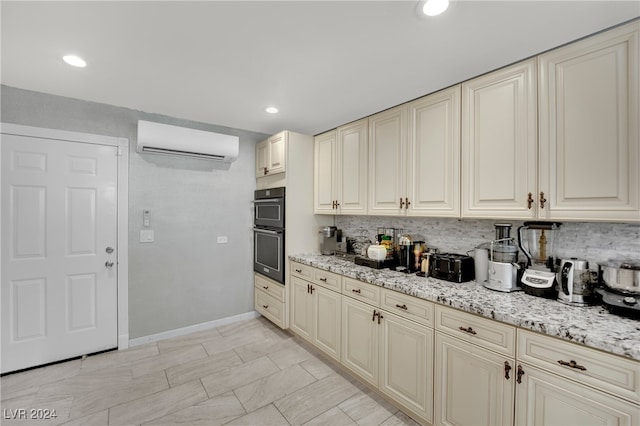 kitchen with tasteful backsplash, light stone countertops, cream cabinetry, double oven, and a wall mounted AC