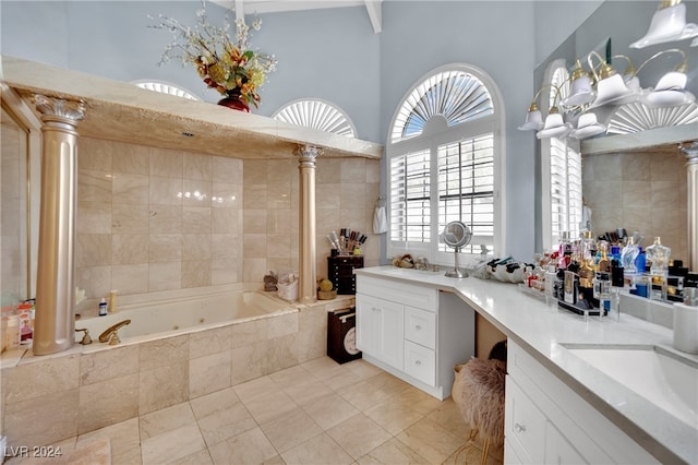 bathroom with a towering ceiling, decorative columns, tiled tub, vanity, and a chandelier