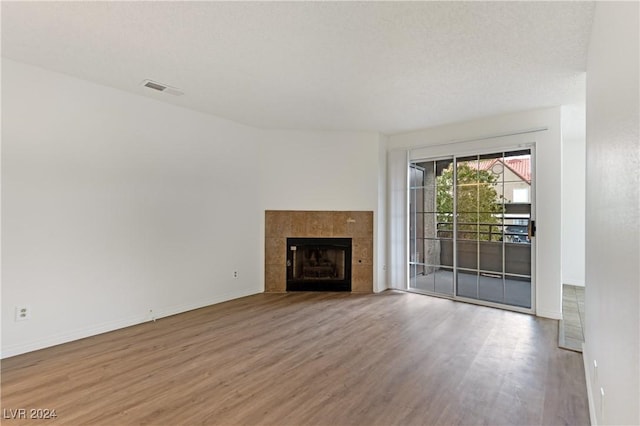 unfurnished living room with a tiled fireplace, wood-type flooring, and a textured ceiling