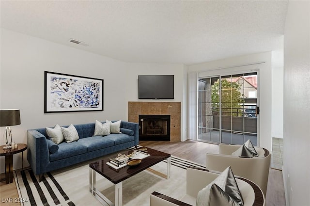 living room with a textured ceiling, a tile fireplace, and light hardwood / wood-style flooring