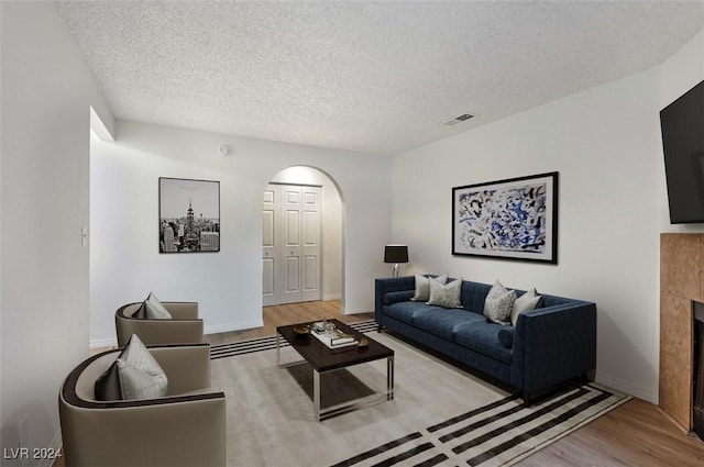 living room with a fireplace, a textured ceiling, and light wood-type flooring