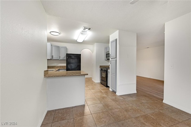 kitchen with kitchen peninsula, black appliances, a textured ceiling, and light hardwood / wood-style floors