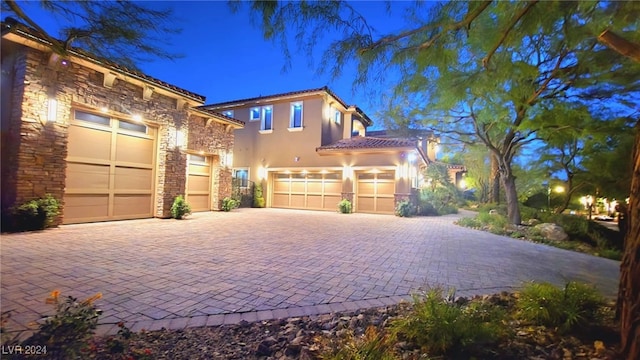 view of front of property with stucco siding, decorative driveway, stone siding, a garage, and a tiled roof