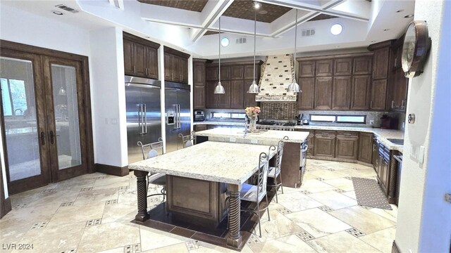 kitchen with visible vents, a center island, stainless steel built in refrigerator, coffered ceiling, and wall chimney exhaust hood