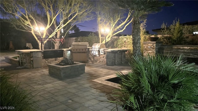 patio at night featuring grilling area and an outdoor kitchen