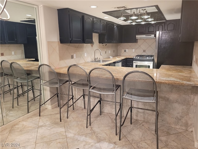 kitchen featuring sink, stainless steel gas range oven, black fridge, kitchen peninsula, and a breakfast bar