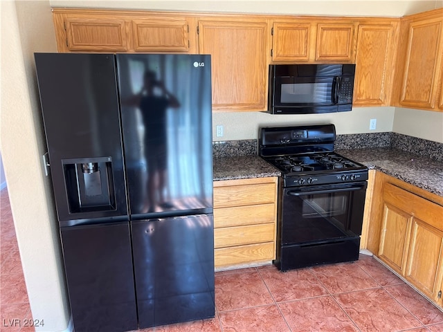 kitchen featuring tile patterned floors, black appliances, and dark stone countertops