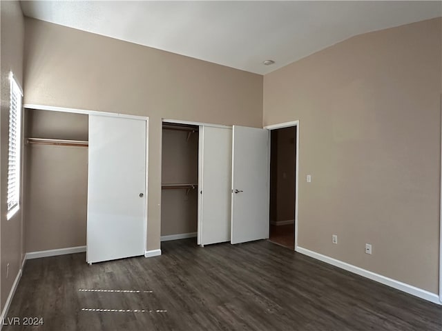 unfurnished bedroom featuring dark wood-type flooring, multiple closets, and lofted ceiling