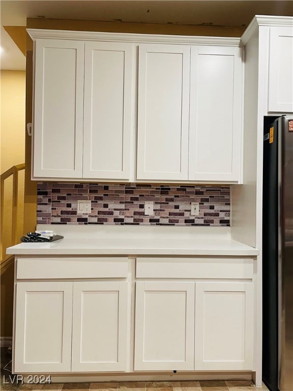 interior space featuring tasteful backsplash, stainless steel refrigerator, and white cabinets