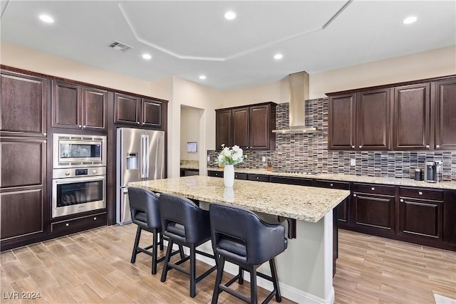 kitchen featuring a kitchen breakfast bar, wall chimney range hood, a center island, and appliances with stainless steel finishes