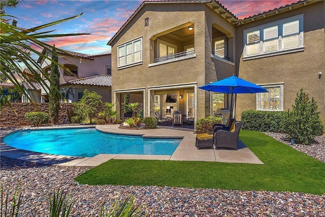 back house at dusk featuring a fenced in pool and a patio area