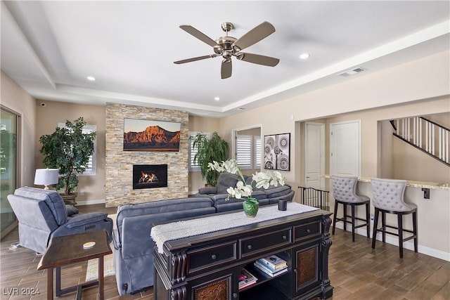 living room with ceiling fan, a raised ceiling, and a fireplace