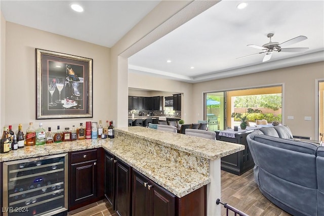 kitchen with ceiling fan, light stone counters, kitchen peninsula, and wine cooler