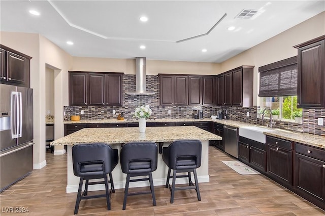 kitchen featuring a kitchen island, appliances with stainless steel finishes, wall chimney exhaust hood, and sink