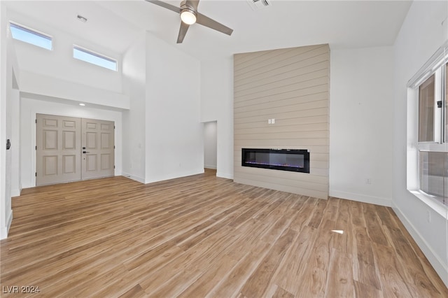 unfurnished living room with a high ceiling, a large fireplace, light wood-type flooring, and ceiling fan