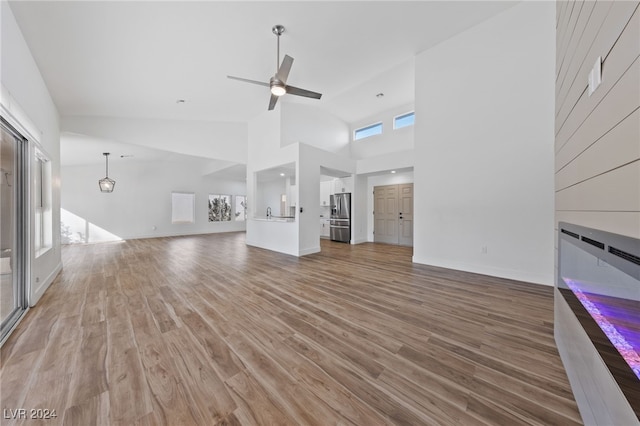 unfurnished living room with hardwood / wood-style flooring, high vaulted ceiling, and ceiling fan