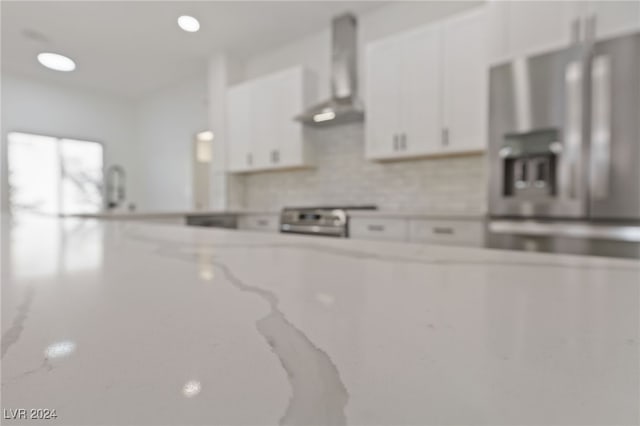 kitchen with tasteful backsplash, white cabinets, stove, stainless steel fridge with ice dispenser, and wall chimney range hood