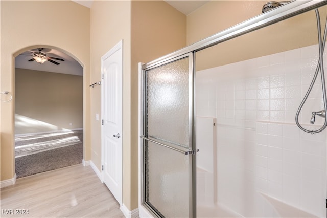 bathroom with hardwood / wood-style floors, a shower with shower door, and ceiling fan