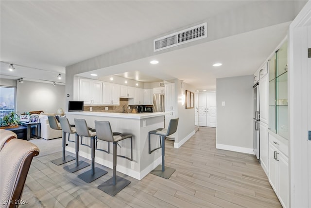 kitchen with kitchen peninsula, high end refrigerator, white cabinetry, a kitchen bar, and light hardwood / wood-style floors