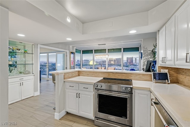 kitchen with light wood-type flooring, kitchen peninsula, stainless steel stove, decorative light fixtures, and white cabinets