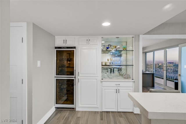 bar with wine cooler, white cabinets, double oven, and light wood-type flooring