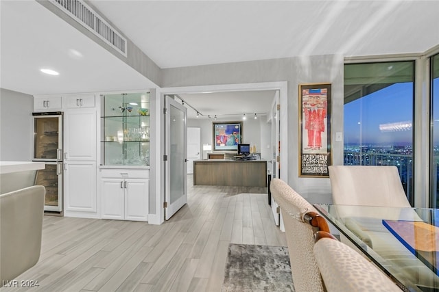 dining space with light hardwood / wood-style floors, beverage cooler, and rail lighting