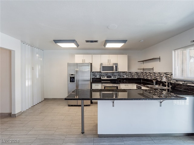 kitchen with kitchen peninsula, appliances with stainless steel finishes, a kitchen breakfast bar, sink, and white cabinets