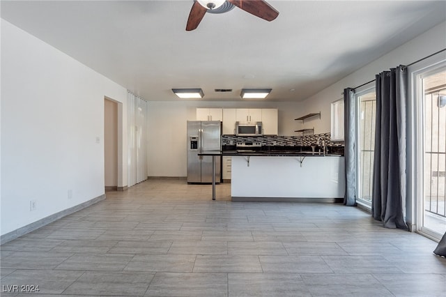 kitchen with kitchen peninsula, stainless steel appliances, ceiling fan, white cabinetry, and a breakfast bar area