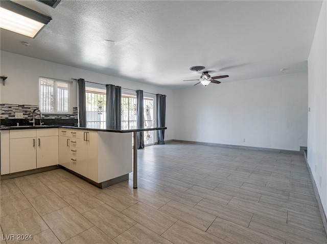 kitchen with sink, decorative backsplash, ceiling fan, a textured ceiling, and kitchen peninsula