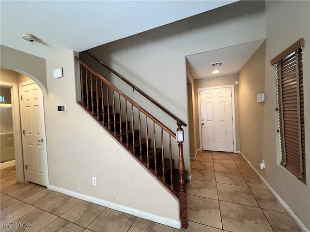 entryway with light tile patterned floors, baseboards, visible vents, and arched walkways